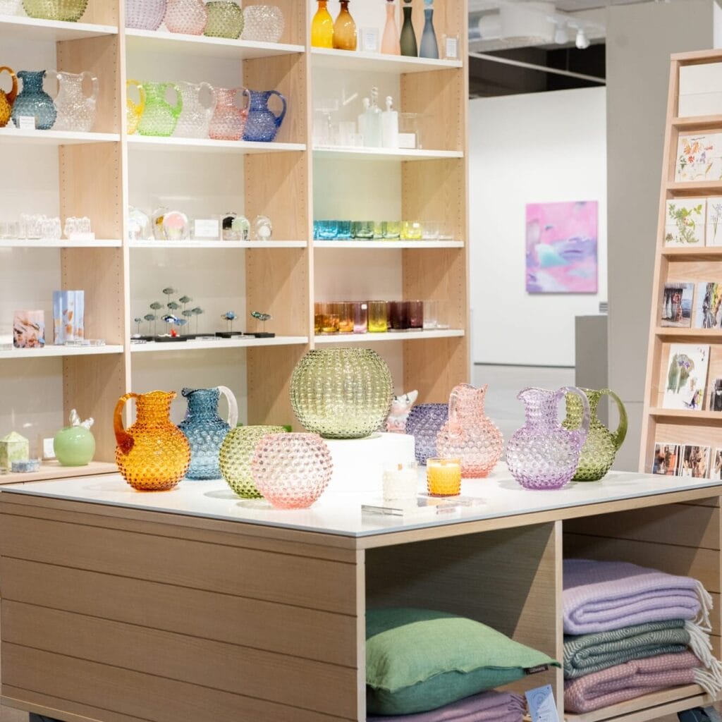 Värikkäitä lasiesineitä ja tyynyjä pöydällä myymälässä.