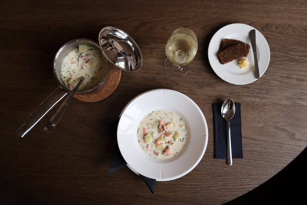 Lohikeitto, ruisleipä ja valkoviini puupöydällä.