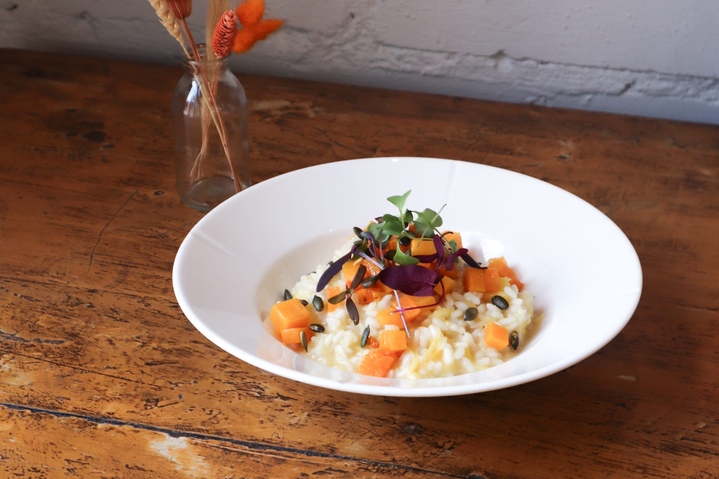 Kurpitsarisotto lautasella, vieressä maljakko.