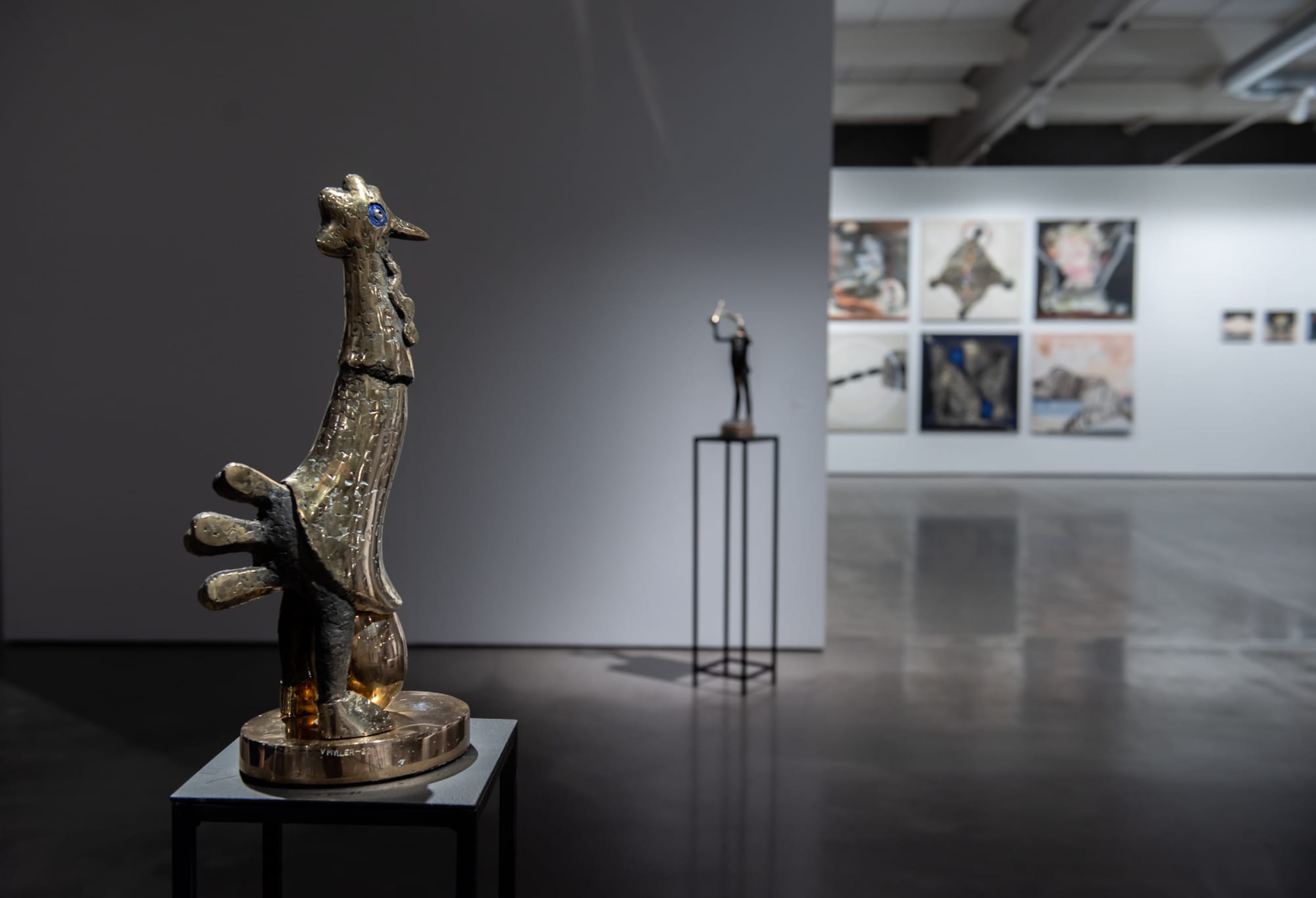 Moderni veistos taidenäyttelyssä, seinällä tauluja.