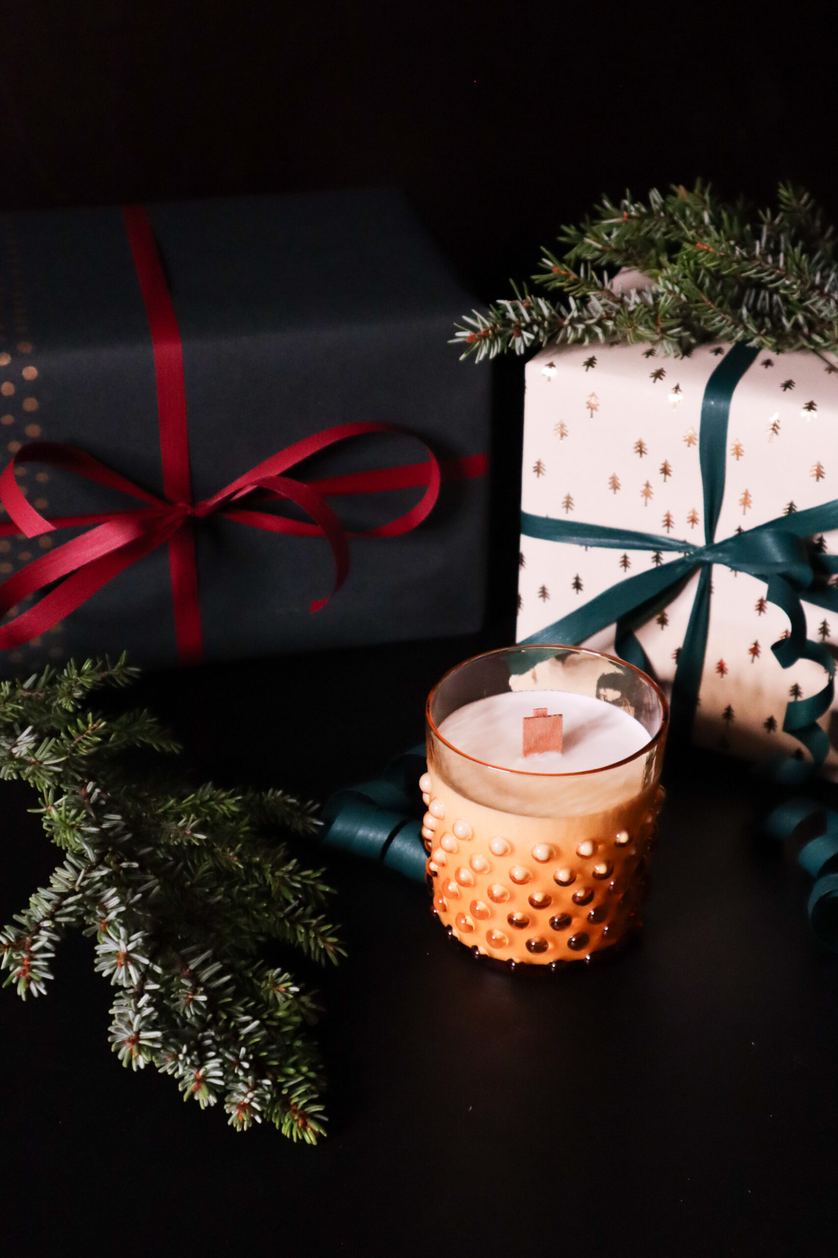 Joululahjat ja kynttilä kuusenoksilla koristettuna.