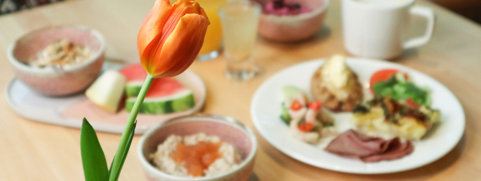 Aamupala pöydällä, keskipisteessä oranssi kukka.