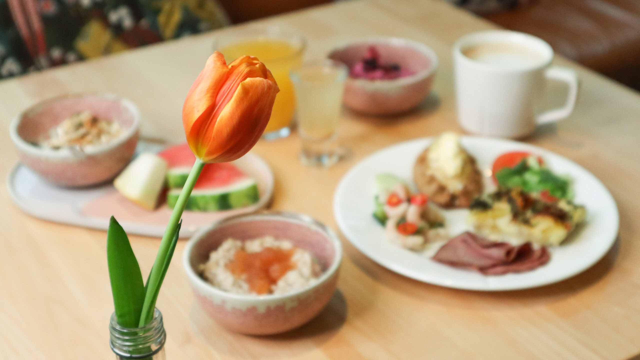 Aamupala pöydällä, keskipisteessä oranssi kukka.