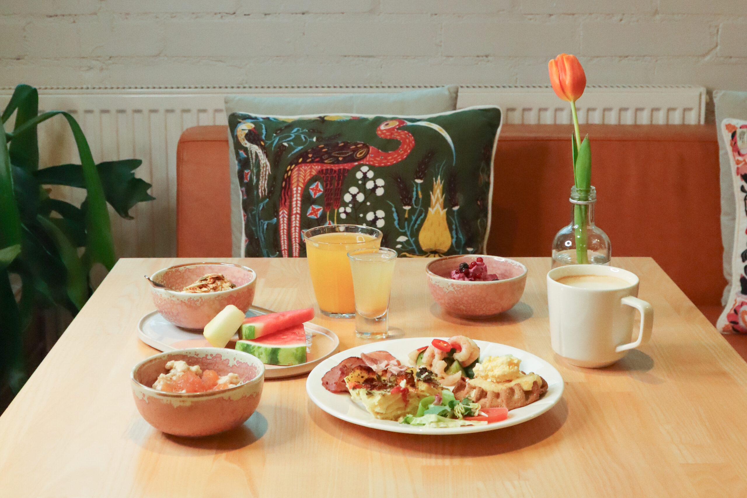 Aamiainen pöydällä: hedelmät, mehu, kahvi, tyyny ja kukka.