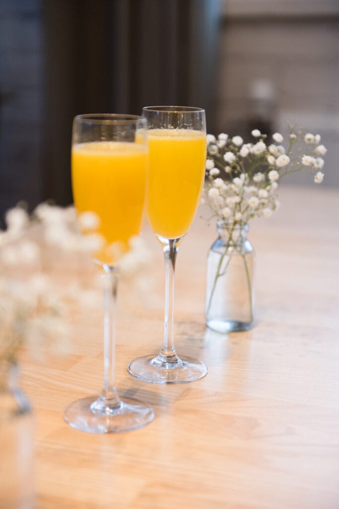 Kaksi lasillista oranssia juomaa pöydällä, kukat mukana