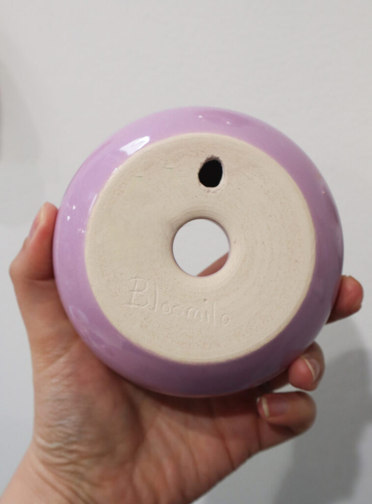 Käden pitelemä violetti keraaminen esine alapuolelta