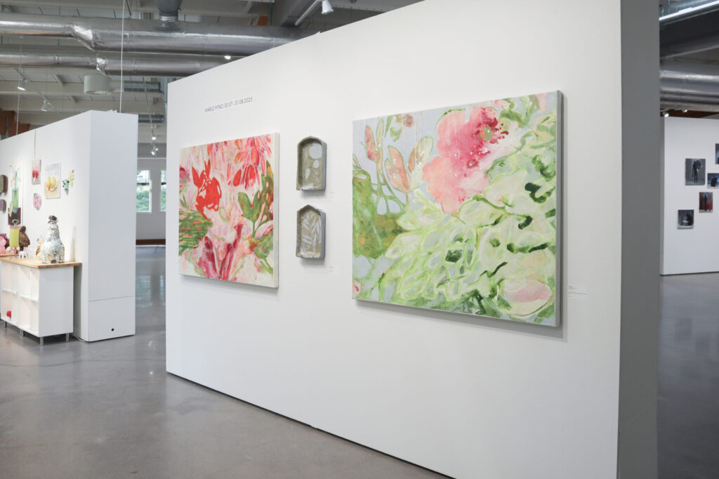 Taidegalleria, värikkäät kukka-aiheiset maalaukset esillä seinällä.
