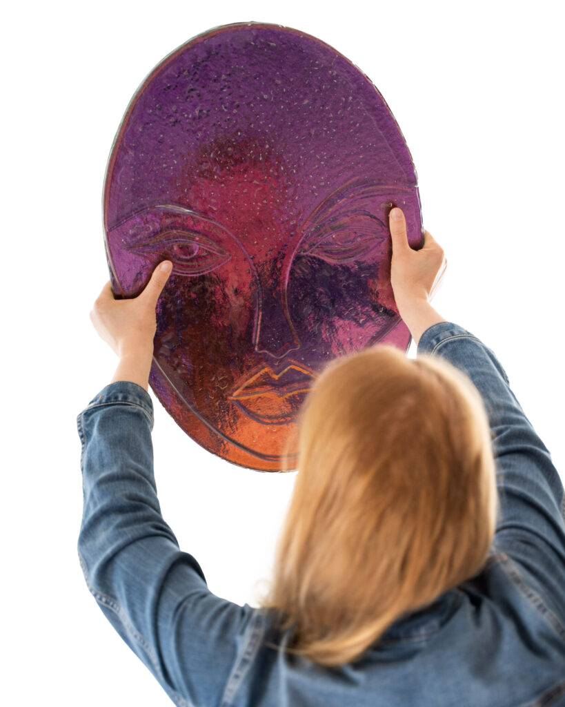 Henkilö nostaa violettia naamion muotoista taideteosta.