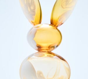 Keltainen lasipupu marmorijalustalla taide-esineenä.