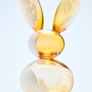 Keltainen lasipupu marmorijalustalla taide-esineenä.