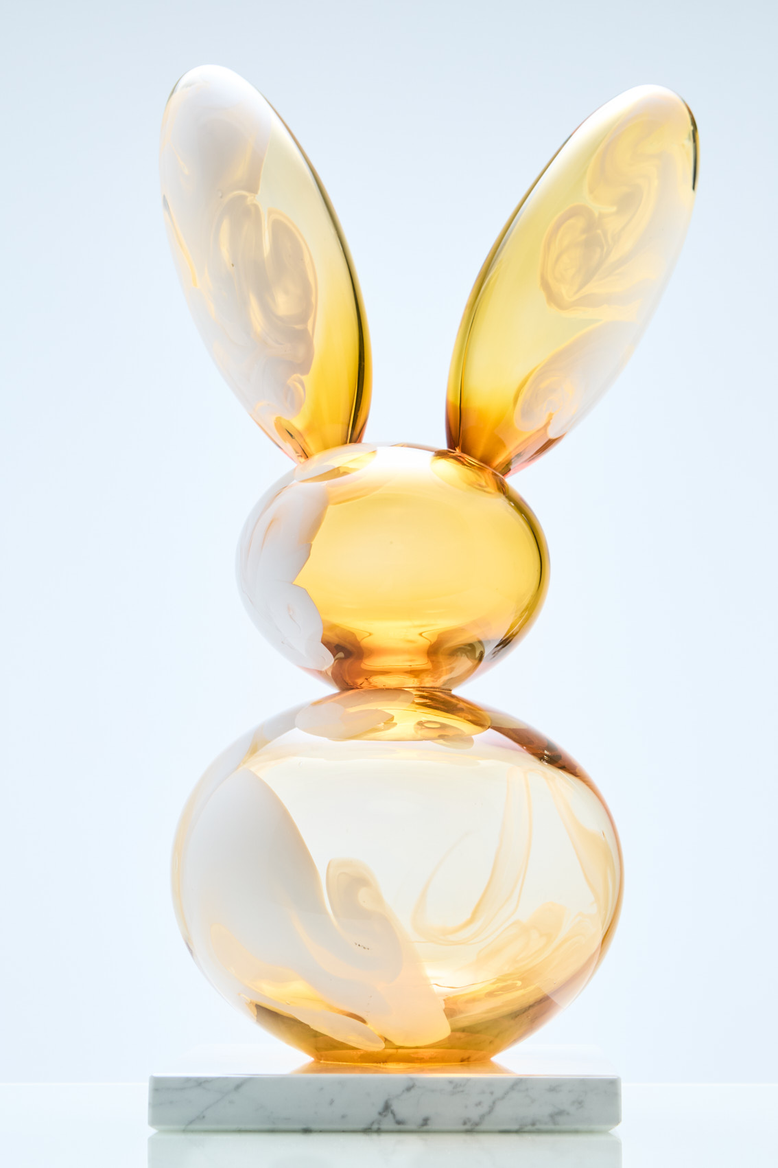 Keltainen lasipupu marmorijalustalla taide-esineenä.
