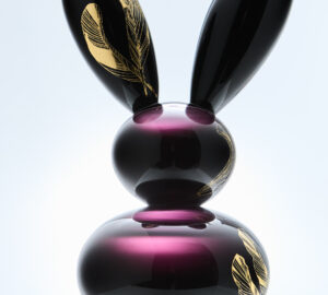 Violetti lasipupu kultaisilla höyhenkuvioilla alustalla.