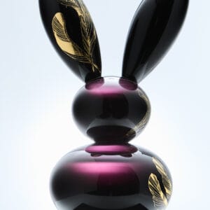 Violetti lasipupu kultaisilla höyhenkuvioilla alustalla.