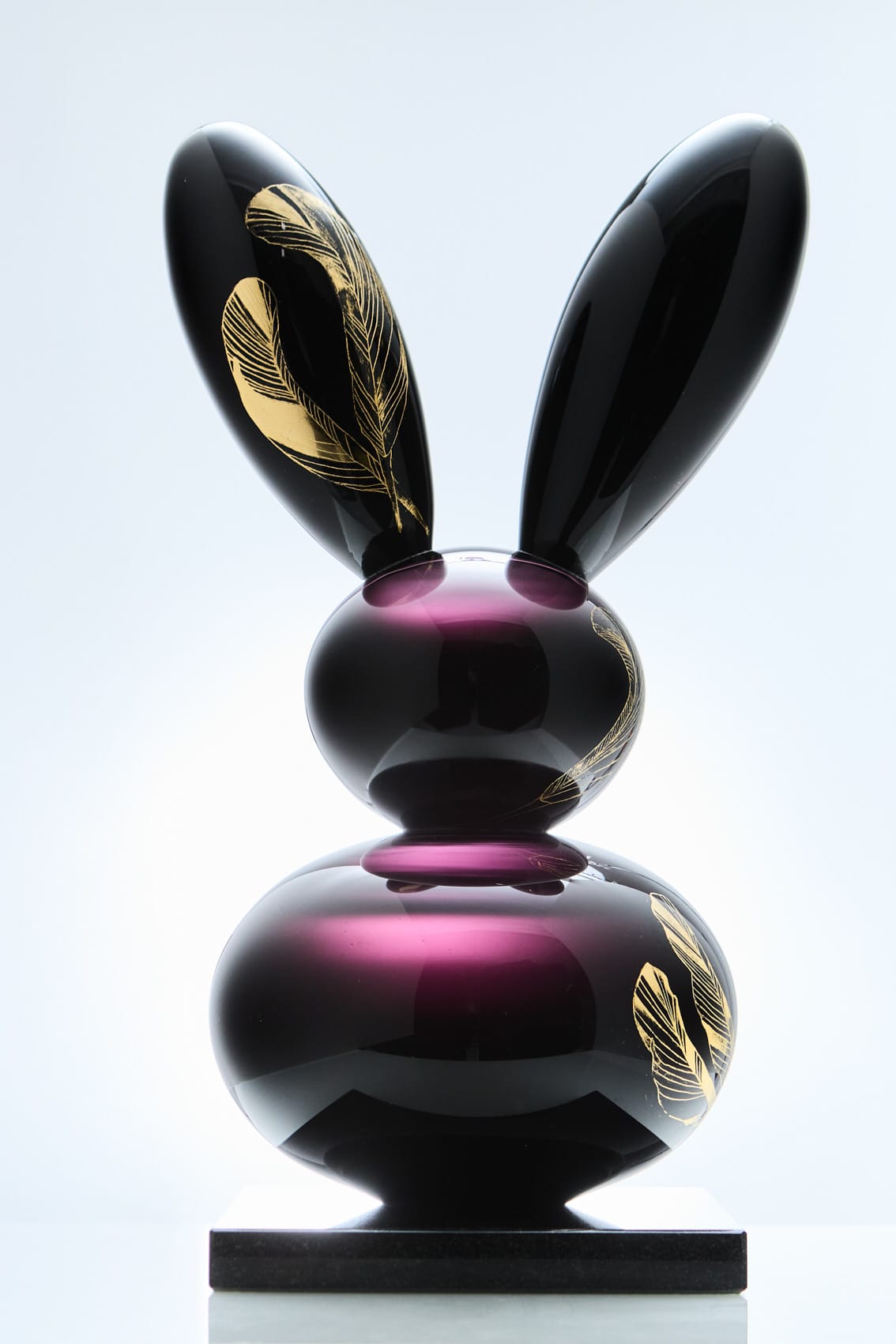 Violetti lasipupu kultaisilla höyhenkuvioilla alustalla.