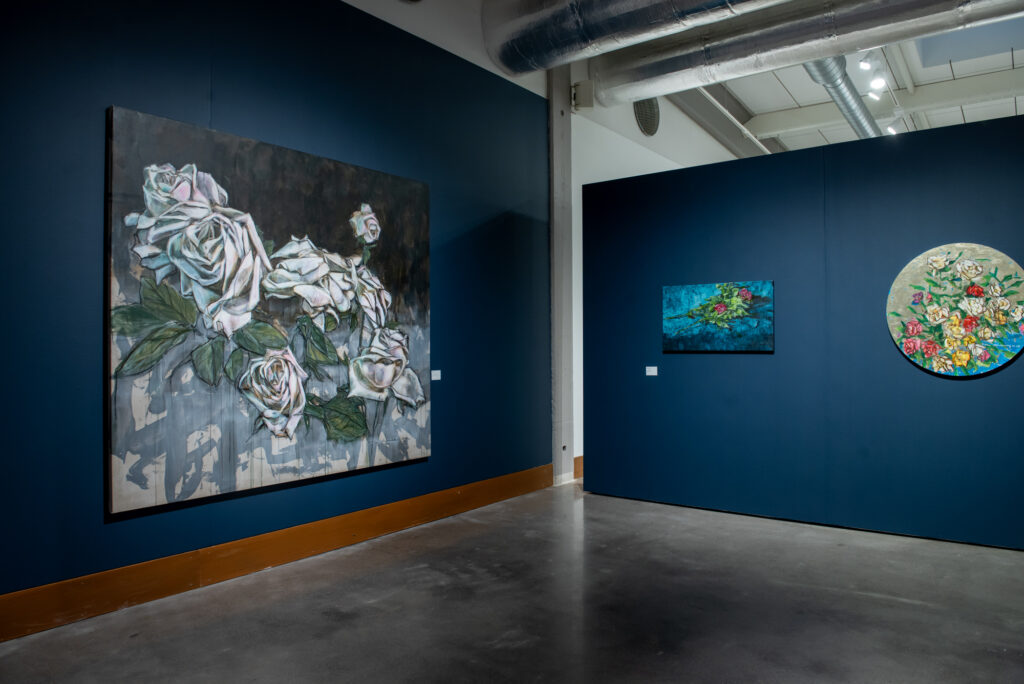 Taidenäyttely, jossa on kukkatauluja tummalla seinällä.