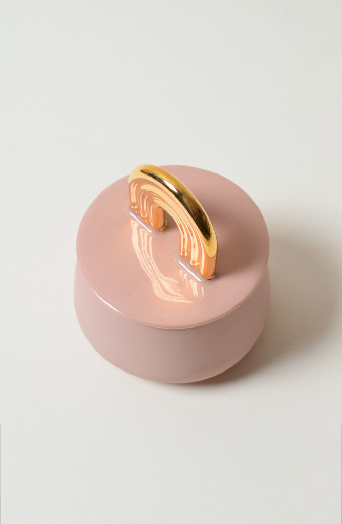 Vaaleanpunainen kannellinen astia kultaisella kahvalla