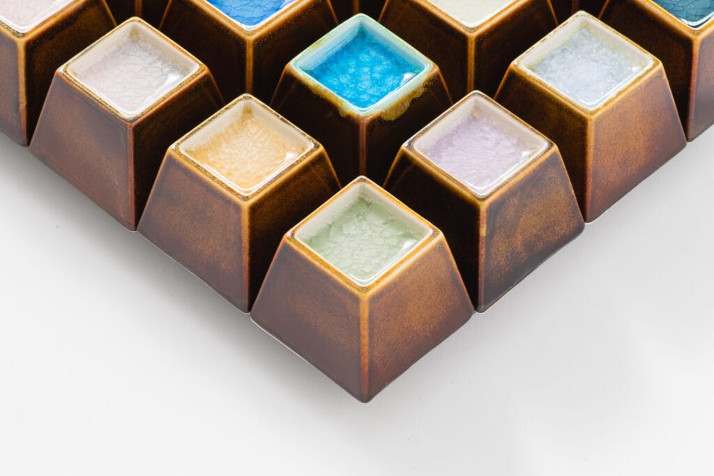 Moniväriset keraamiset palaset järjestettynä ruudukossa.