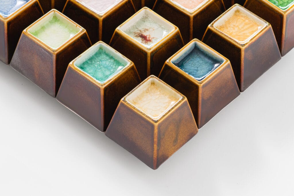 Värikkäät neliönmuotoiset posliinilaatat valkoisella taustalla.