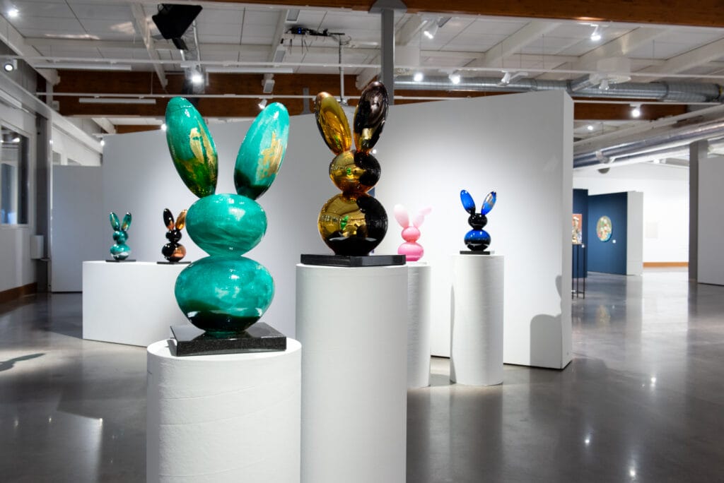 Värikkäät veistokset taidegalleriassa esillä jalustoilla.