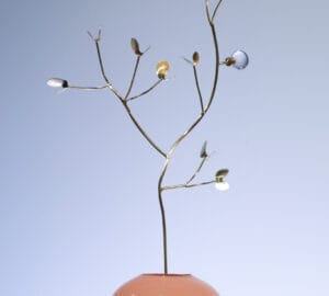 Puunoksaa muistuttava veistos vaaleanpunaisessa maljakossa.