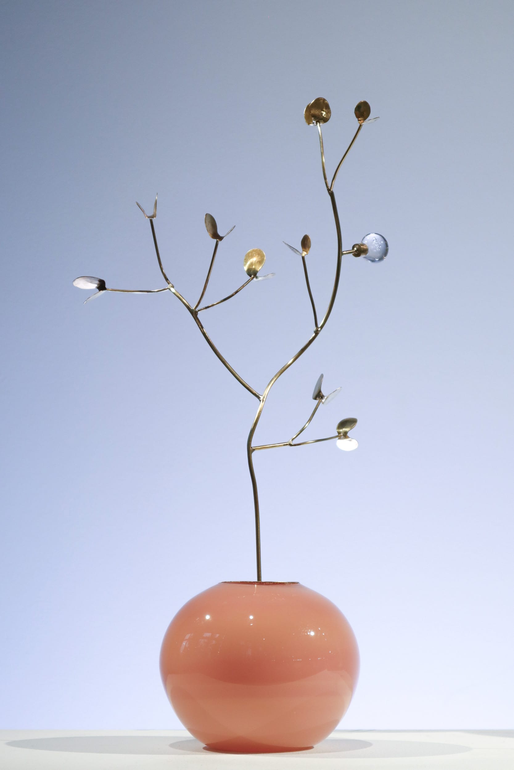 Puunoksaa muistuttava veistos vaaleanpunaisessa maljakossa.