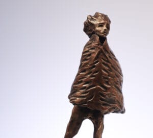 Pronssiveistos persoonasta, paksu veistoksellinen takki päällä.