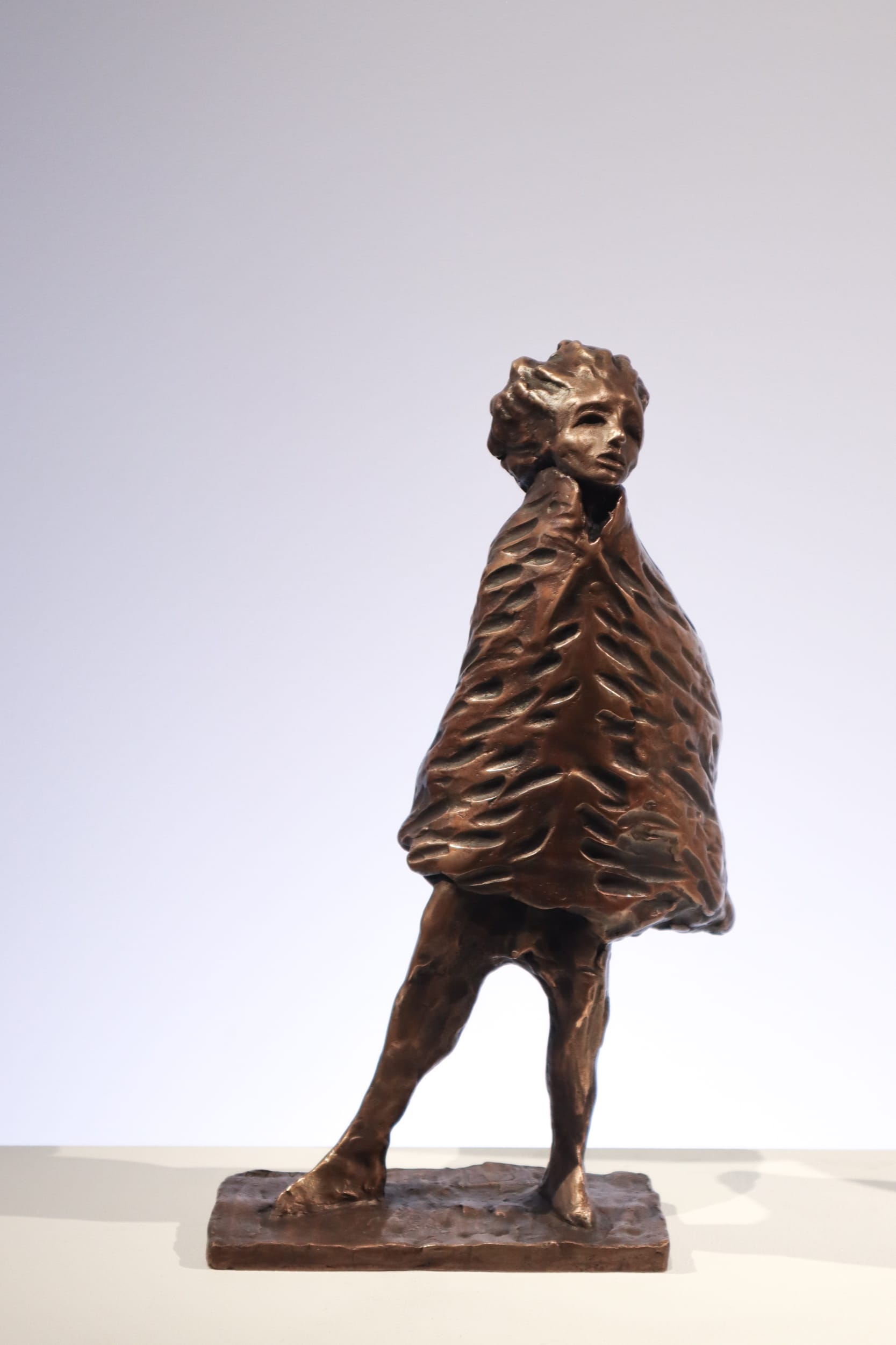 Pronssiveistos persoonasta, paksu veistoksellinen takki päällä.