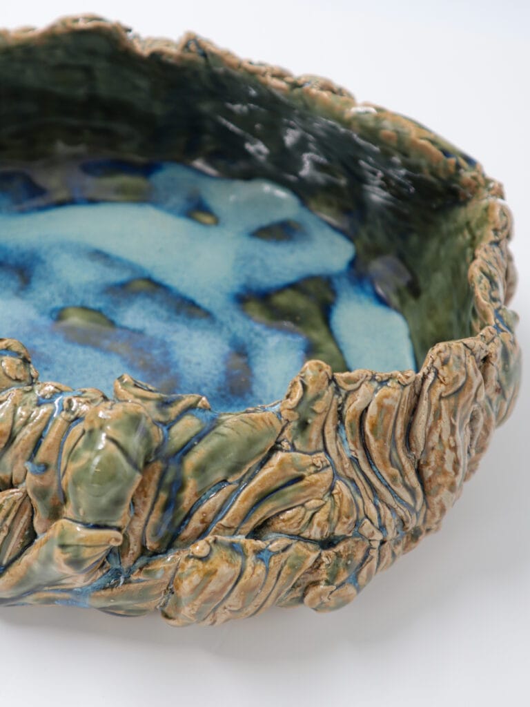 Sininen ja vihreä keraaminen kulho koristeellisilla reunoilla.