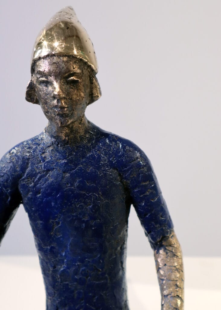 Metalliveistos henkilöstä sinisessä vaatteessa, päässä hattu.