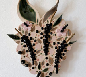 Koristeellinen keraaminen lehti ja marjat seinällä.