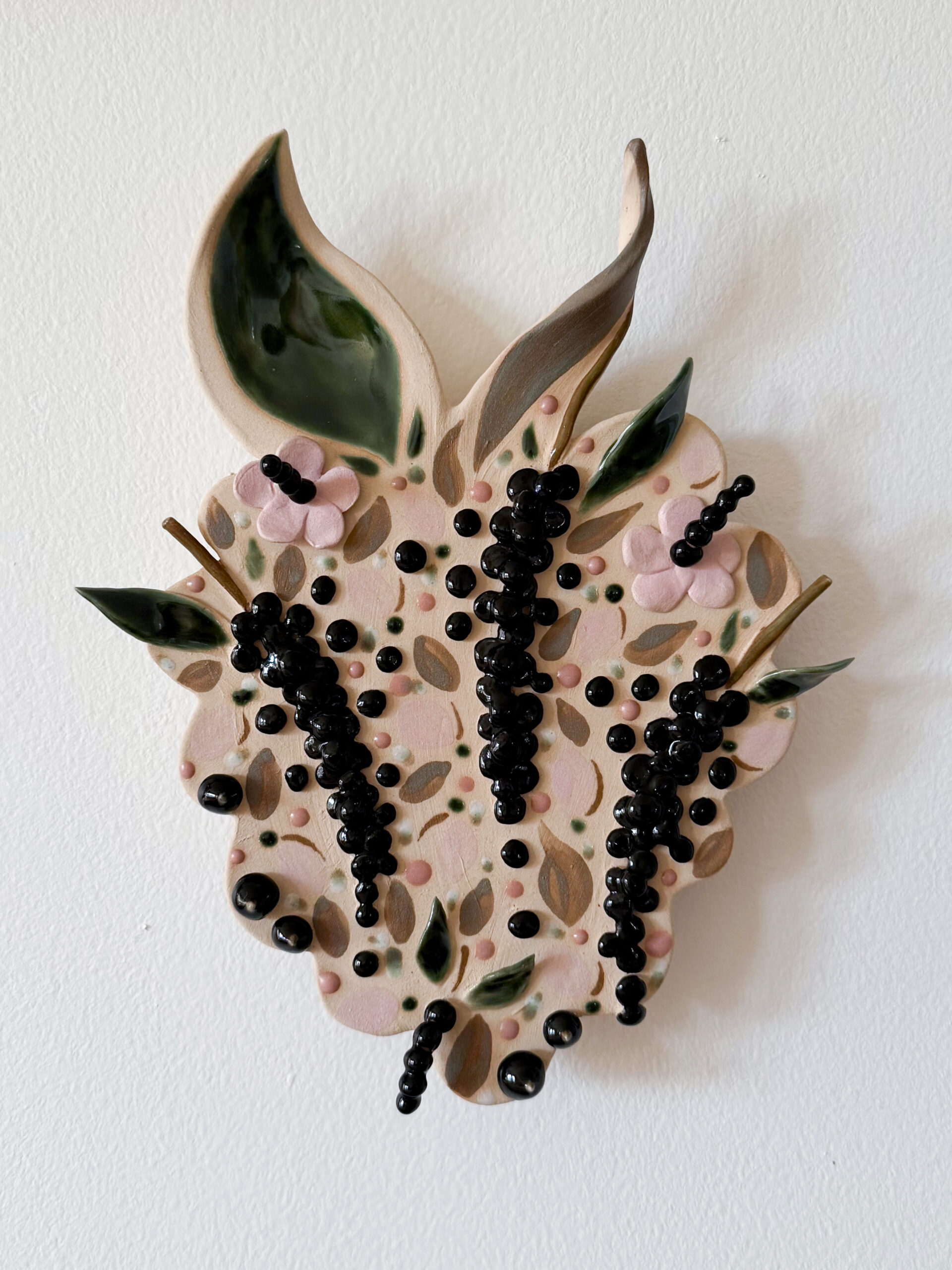 Koristeellinen keraaminen lehti ja marjat seinällä.