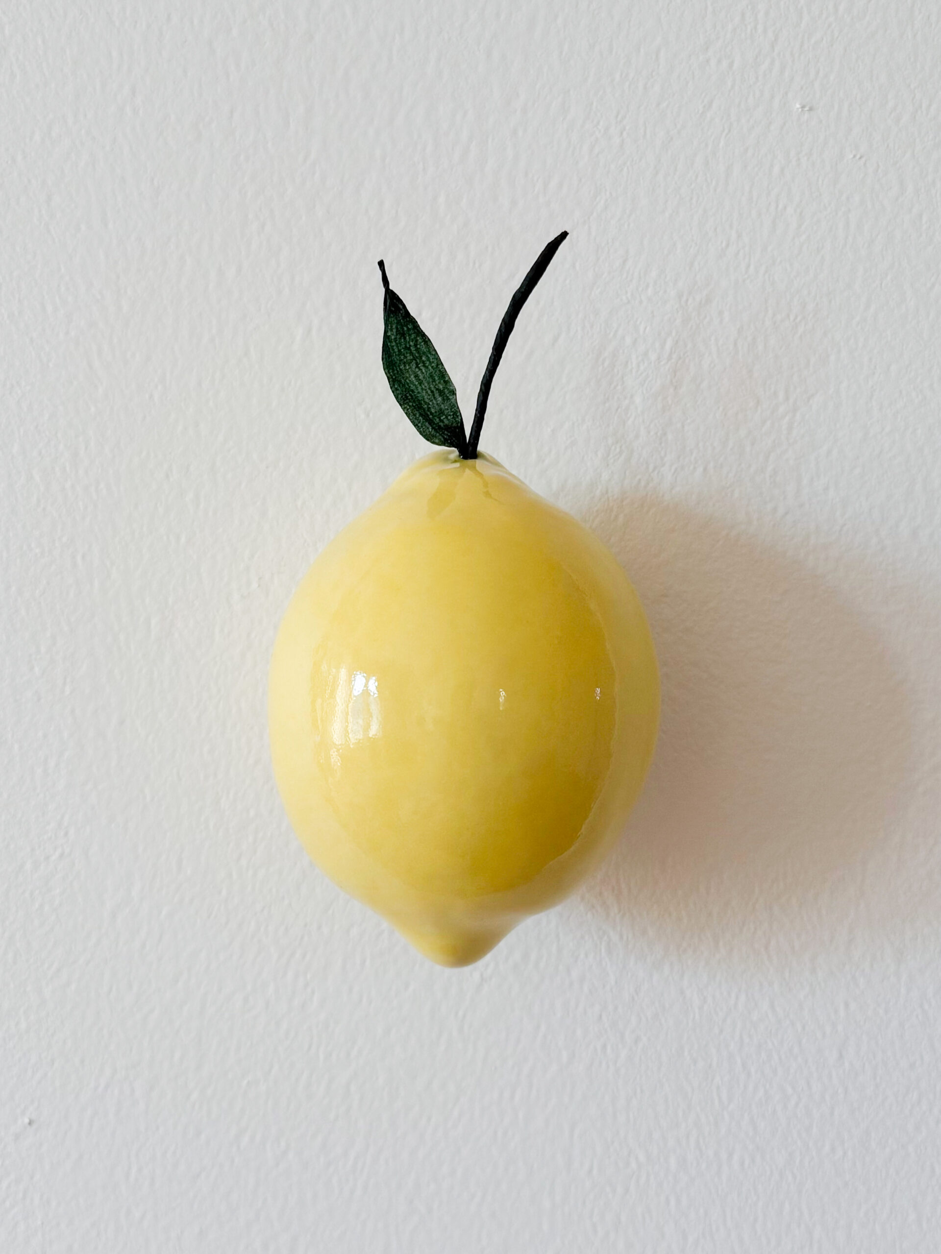 Keltainen sitruuna valkoisella seinällä.