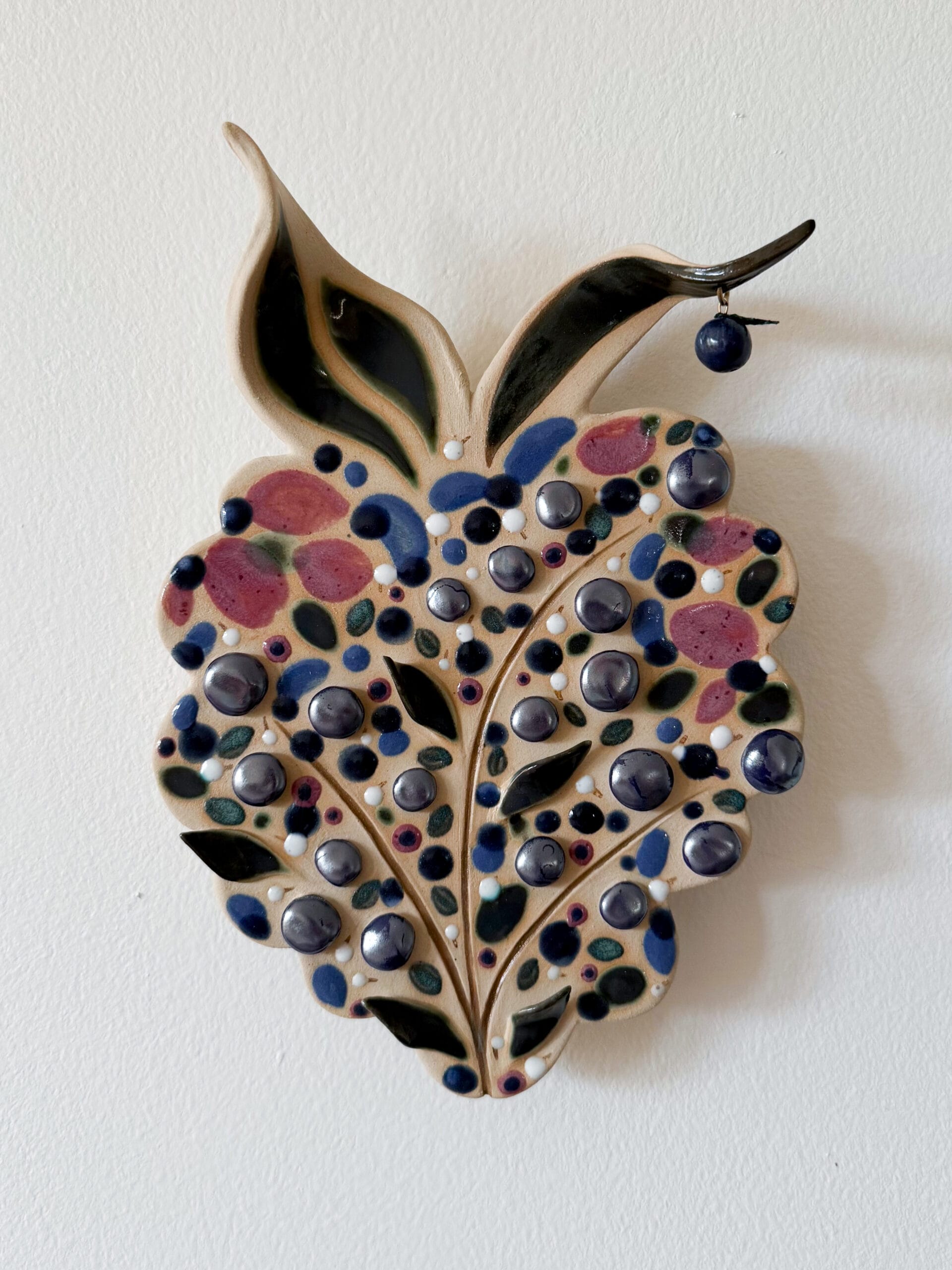 Värikäs keramiikkakoriste lehtimuodossa seinällä.