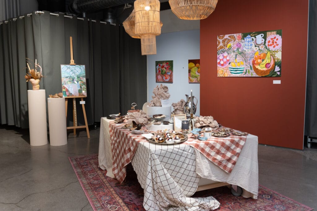 Taidegalleria, pöytä tarjottimilla, värikkäitä maalauksia seinällä.