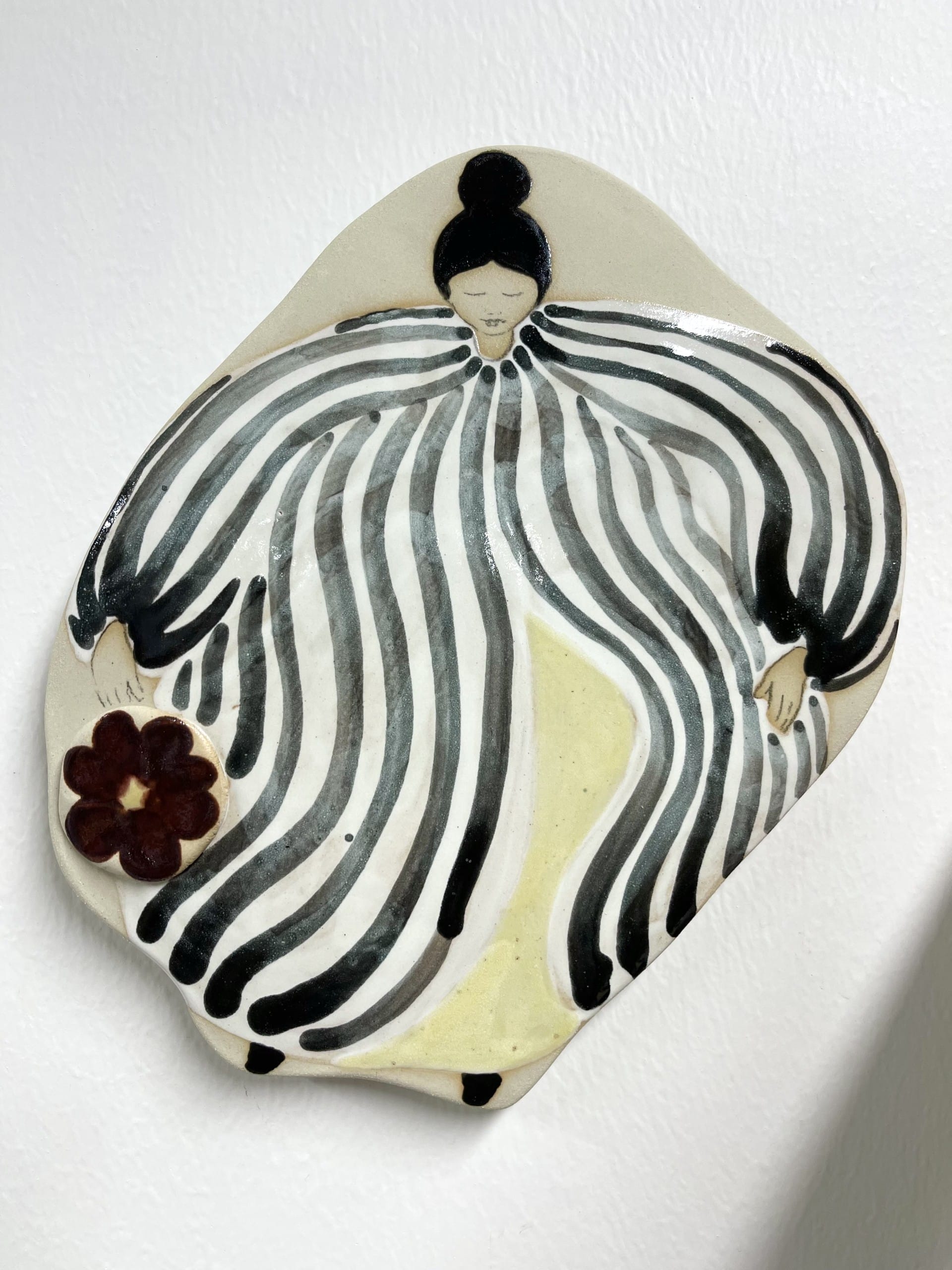 Taiteellinen keramiikkaefekti, mustavalkoraidallinen hahmo, kukka kädessä.