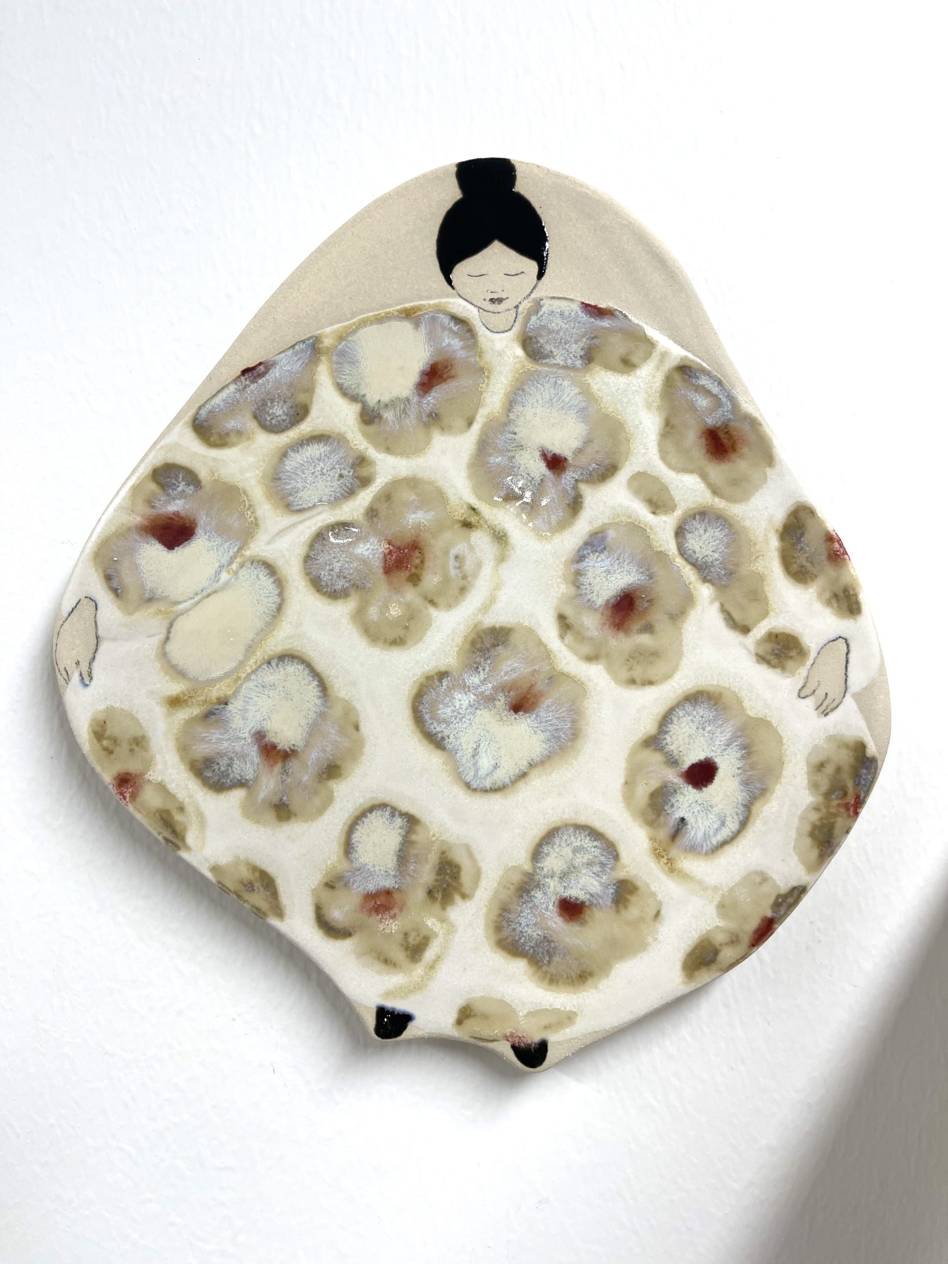 Keraaminen taideteos, kukkakuviolla ja ihmishahmolla.