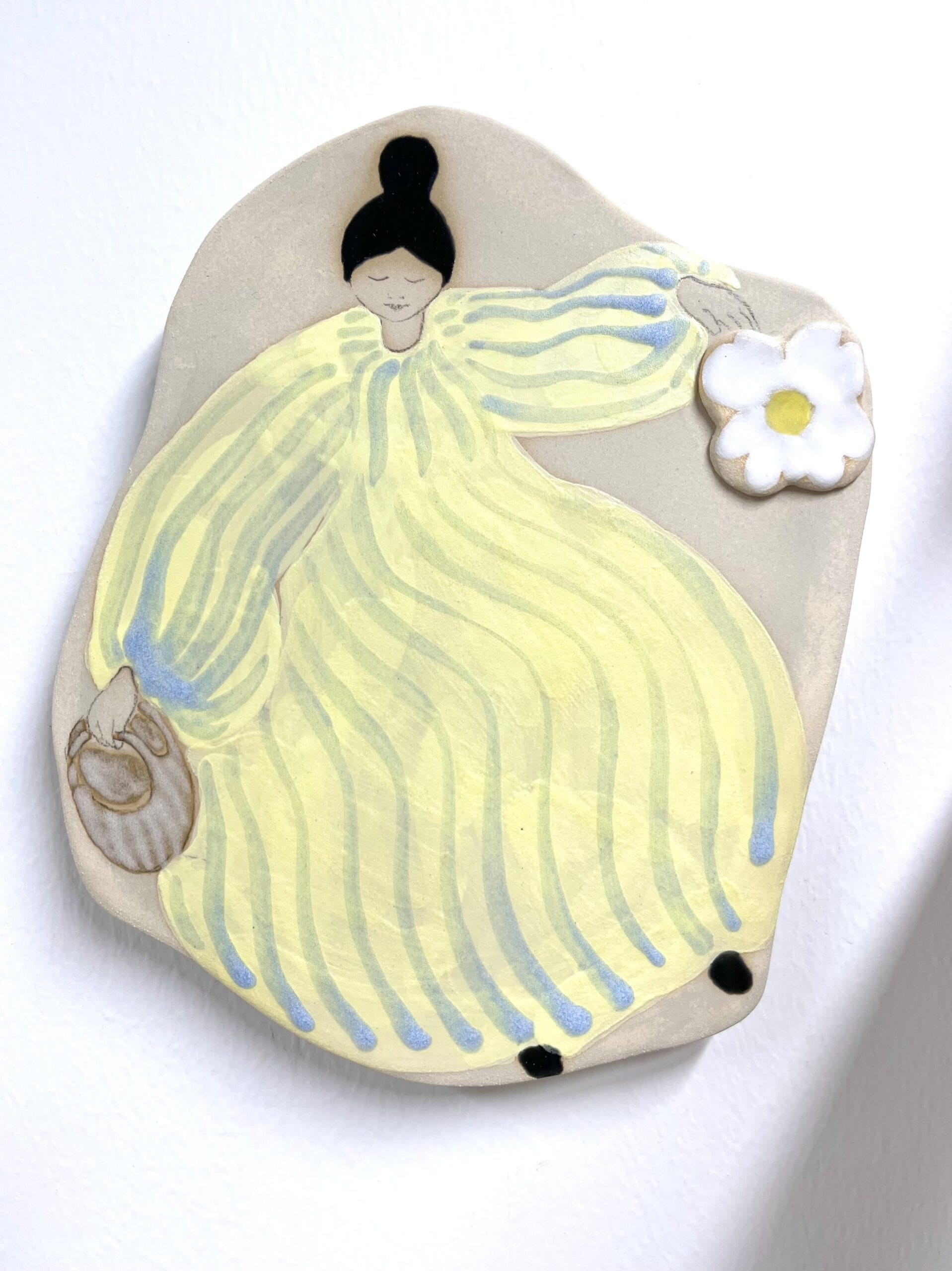 Keltapukuinen hahmo kukka kädessään, savitaide