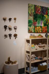 Kasviksia ja sieniä näyttelytilassa hyllyillä.