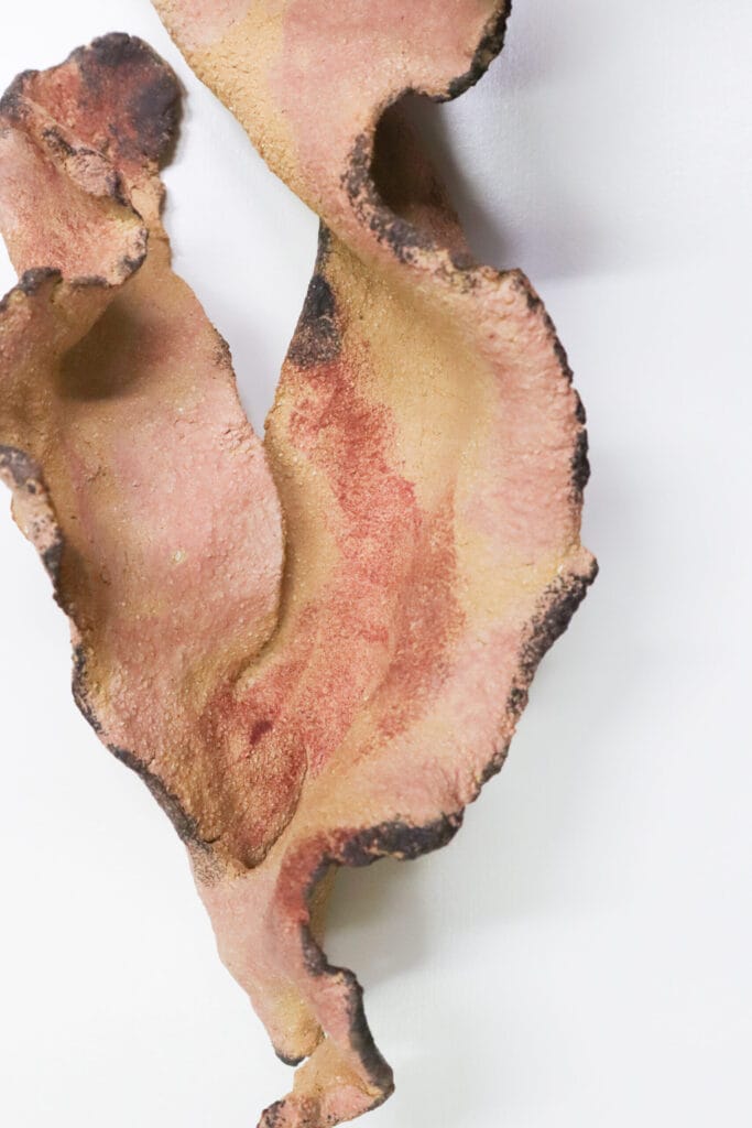 Vaaleanpunainen keraaminen abstrakti veistos valkoisella taustalla.