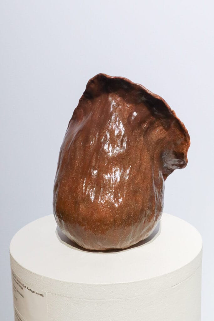 Ruskearaaminen, abstrakti saviveistos jalustalla.