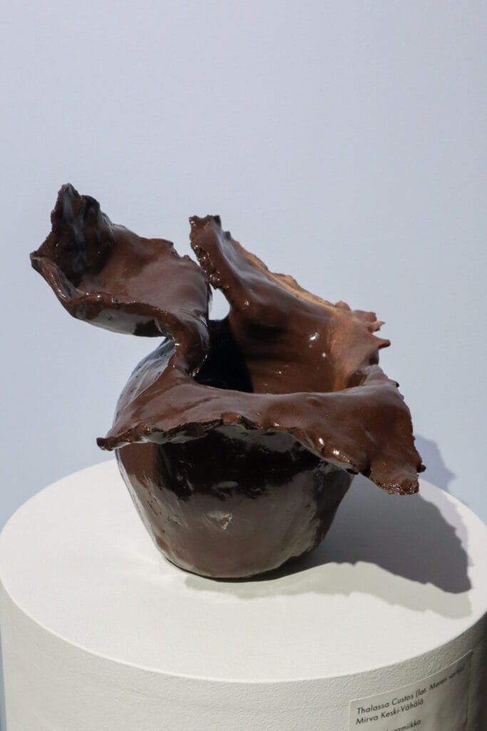 Tummanruskea keraaminen veistos valkoisella alustalla.